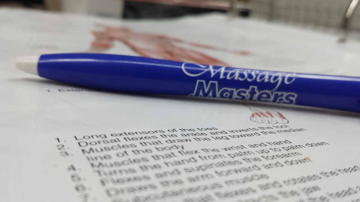 Pen resting on an open anatomy book used in massage continuing education courses
